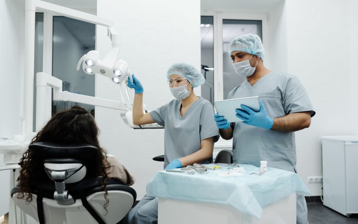 Dentistas em clínica se preparam para procedimento odontológico com paciente sentado, demonstrando trabalho em equipe