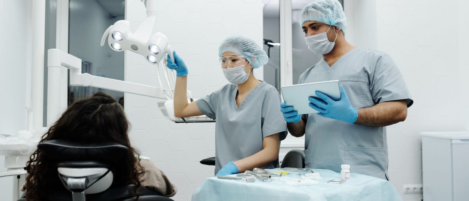 Dentistas em clínica se preparam para procedimento odontológico com paciente sentado, demonstrando trabalho em equipe