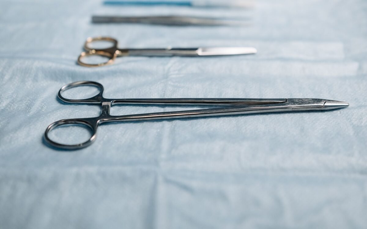 Close-up de instrumentos cirúrgicos incluindo porta-agulha em pano azul em ambiente médico