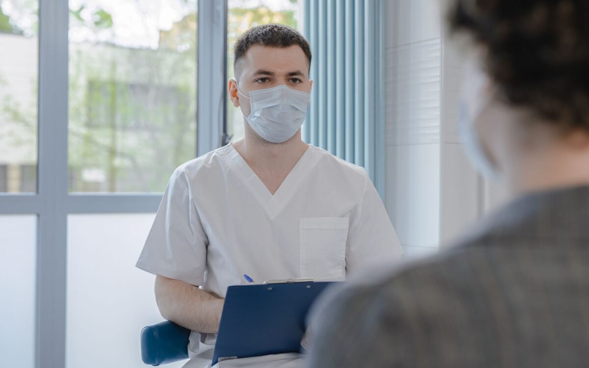 Profissional da saúde em uniforme consultando um paciente enquanto anota informações