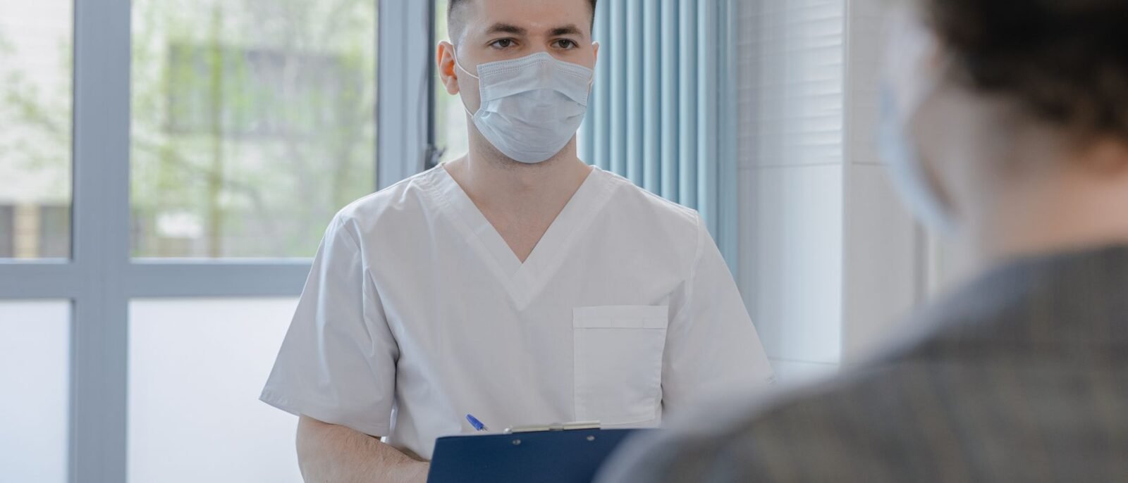 Profissional da saúde em uniforme consultando um paciente enquanto anota informações