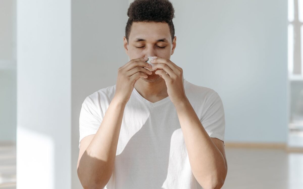 Um homem espirrando em um lenço, ilustrando sintomas de gripe ou alergias