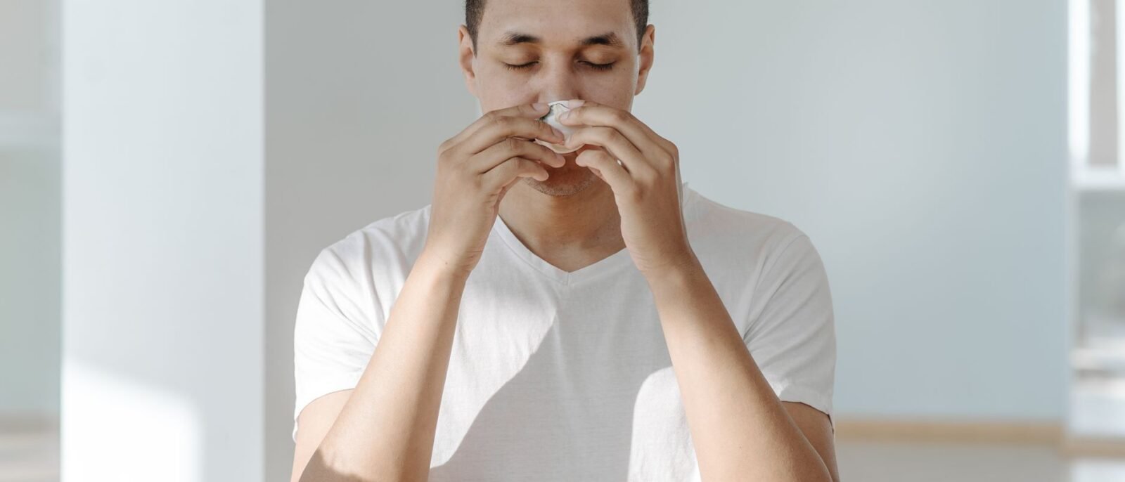 Um homem espirrando em um lenço, ilustrando sintomas de gripe ou alergias